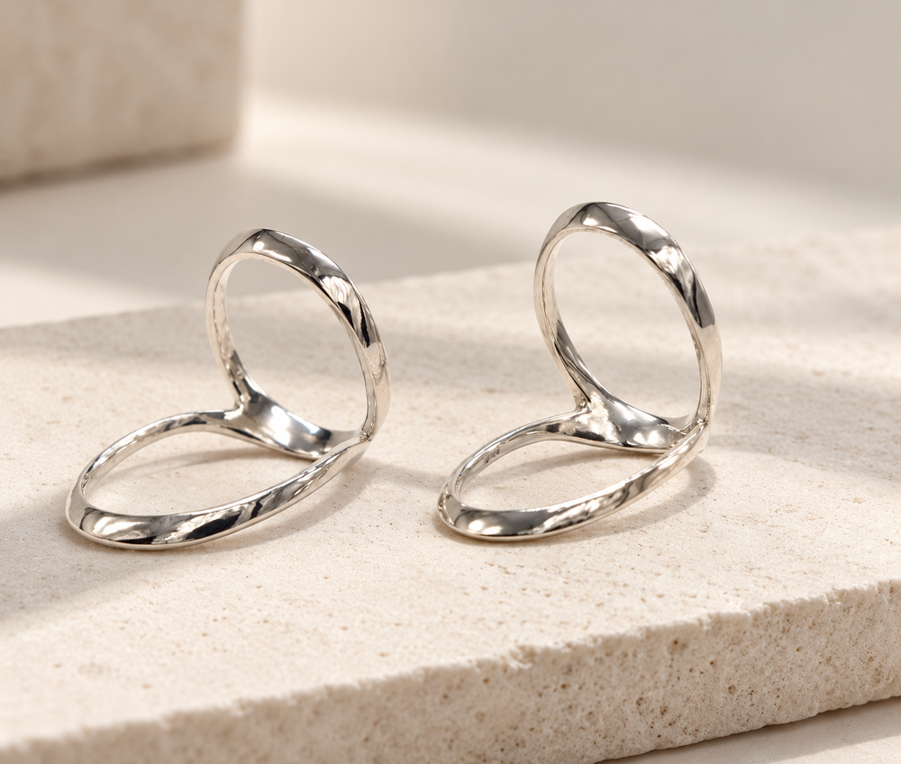 Two swan neck splints with a hammered silver-tone finish standing on a stone surface