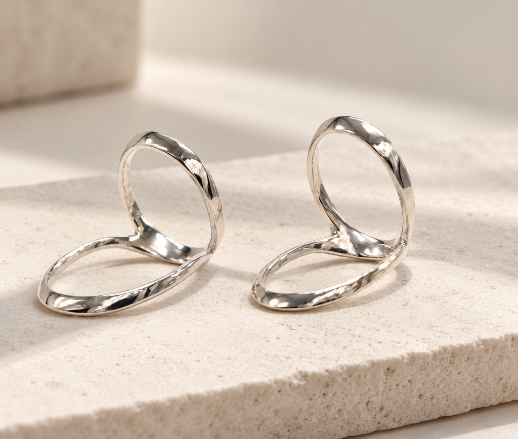 Two swan neck splints with a hammered silver-tone finish standing on a stone surface